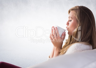 Woman on couch drinking from white mug against white wall