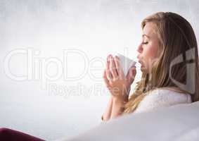 Woman on couch drinking from white mug against white wall