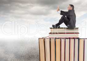 Man sitting on Books stacked by grey cloudy sky
