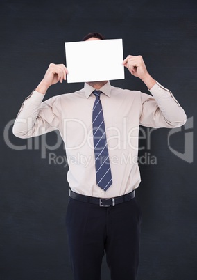 Business man holding card over face against navy chalkboard