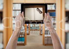 Hands with tablet showing open book and glasses against blurry archways