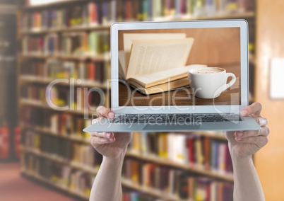Hands with laptop showing book and coffee against blurry bookshelf