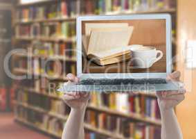 Hands with laptop showing book and coffee against blurry bookshelf