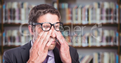 Business man rubbing eyes against blurry bookshelf