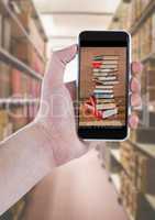 Hand with phone showing book pile against blurry bookshelfs