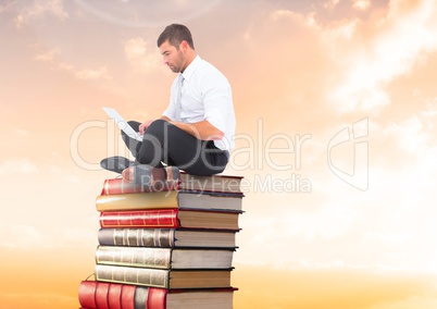Businessman sitting on Books stacked by sunset with laptop