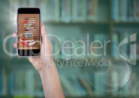 Hand with phone showing book pile against blurry bookshelf with green overlay and flare