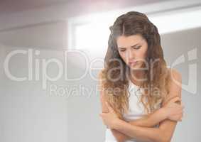 Sad young woman holding herself against window light
