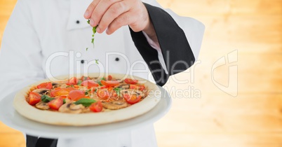 Chef putting herbs on pizza against blurry yellow wood panel
