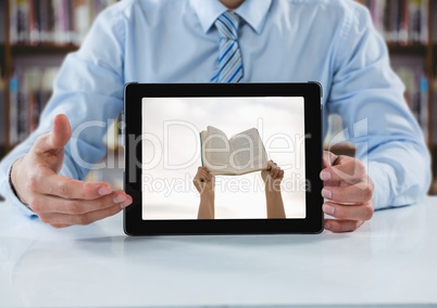 Business man at table with tablet showing hands with book against blurry bookshelf