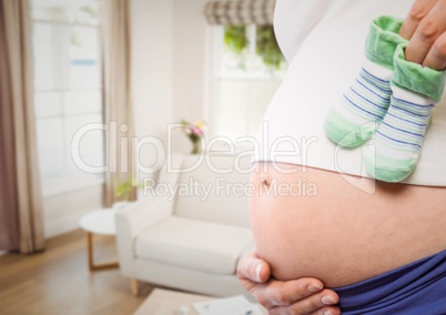 Pregnant woman mid section holding socks against blurry sitting room