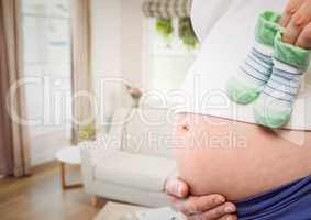 Pregnant woman mid section holding socks against blurry sitting room