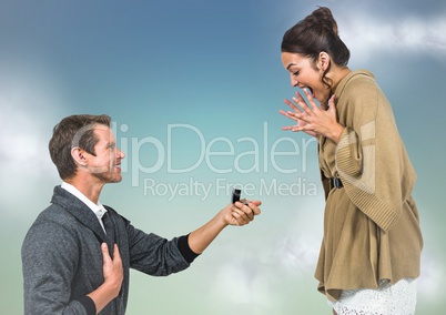 Man propsing to woman against blue green background with clouds