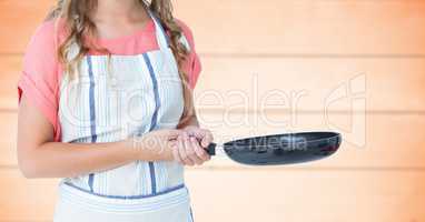 Woman in apron with frying pan on against blurry orange wood panel