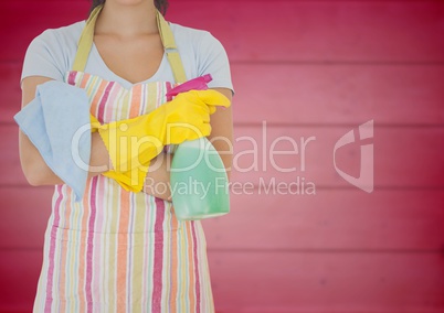 Woman in apron with arms folded and cleaner against blurry pink wood panel