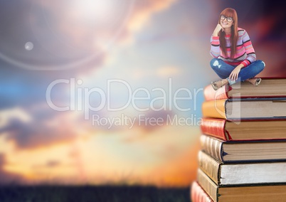 Woman sitting on Books stacked by sunset sky