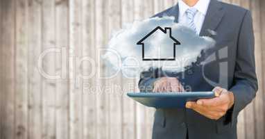 Business man with tablet and cloud with house against blurry wood background