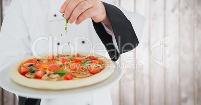 Chef putting herbs on pizza against blurry wood panel