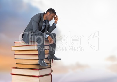 Businessman sitting onBooks stacked by cloudy sky