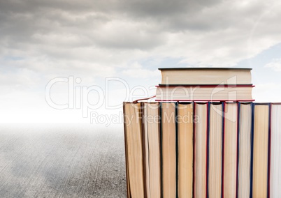 Books stacked by grey cloudy sky