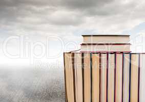 Books stacked by grey cloudy sky