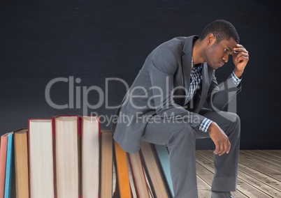 Young man upset sitting on Books stacked by blackboard