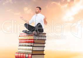 Businessman meditating sitting on Books stacked by sunset with laptop