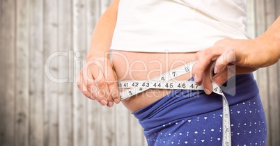 Pregnant woman mid section with measuring tape against blurry wood panel