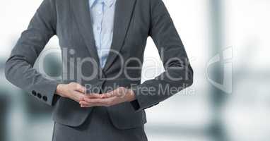 Business woman mid section with hands together in blurry grey office