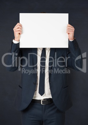 Business man with blank card over face against navy chalkboard