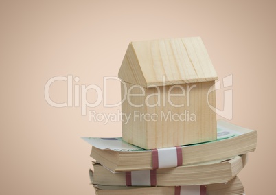 Wooden house sitting on money pile notes against beige background