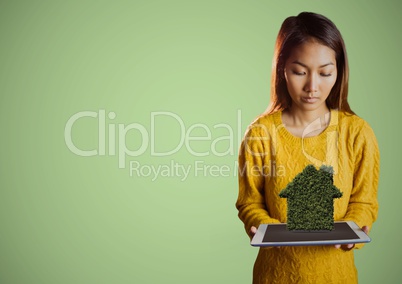 Woman looking down at tablet and shrub house against green background