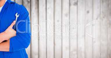 Mechanic with arms folded and wrench against blurry wood panel