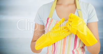 Woman in apron with yellow gloves on against blurry grey wood panel