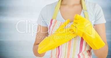 Woman in apron with yellow gloves on against blurry grey wood panel