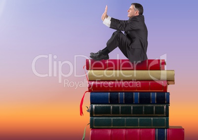 Businessman sitting on Books stacked by twilight sky