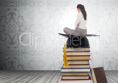 Woman sitting on Books stacked by decorative wallpaper with graduation hat