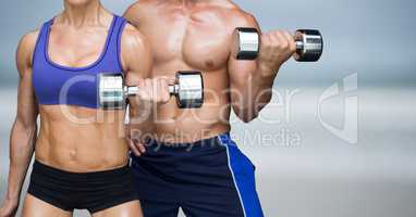 Man and woman weight lifting on blurry beach