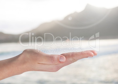 Open palm hand in front of ocean and mountains