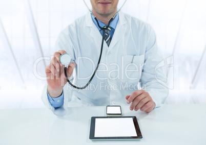 Doctor with stethoscope and devices at desk against blurry window