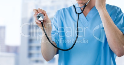 Nurse with stethoscope mid section against blurry buildings