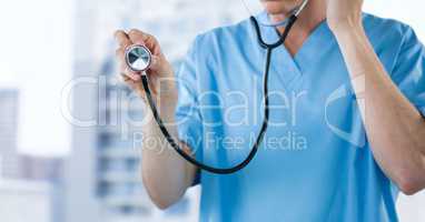 Nurse with stethoscope mid section against blurry buildings