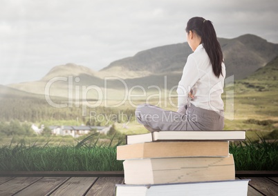 Woman sitting on Books stacked by landscape mountains