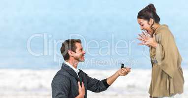 Man propsing to woman against blurry beach