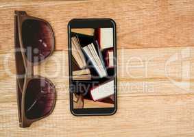 Sunglasses and phone showing standing books