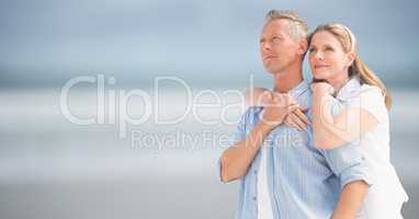 Woman with arms around man against blurry beach