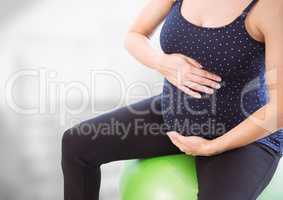 Pregnant woman mid section on excercize ball against blurry grey background