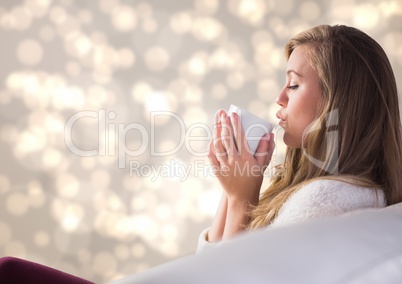 Woman on couch drinking from white mug against cream bokeh