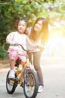 Child learning to bike with help of mother outdoor.