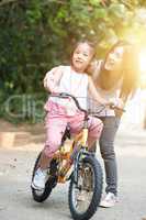 Mother helping daughter learn biking outdoor.